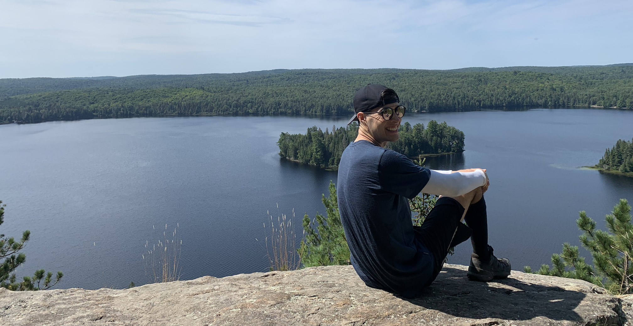 Daniel sitting on an outcropping that looks out over a lake.